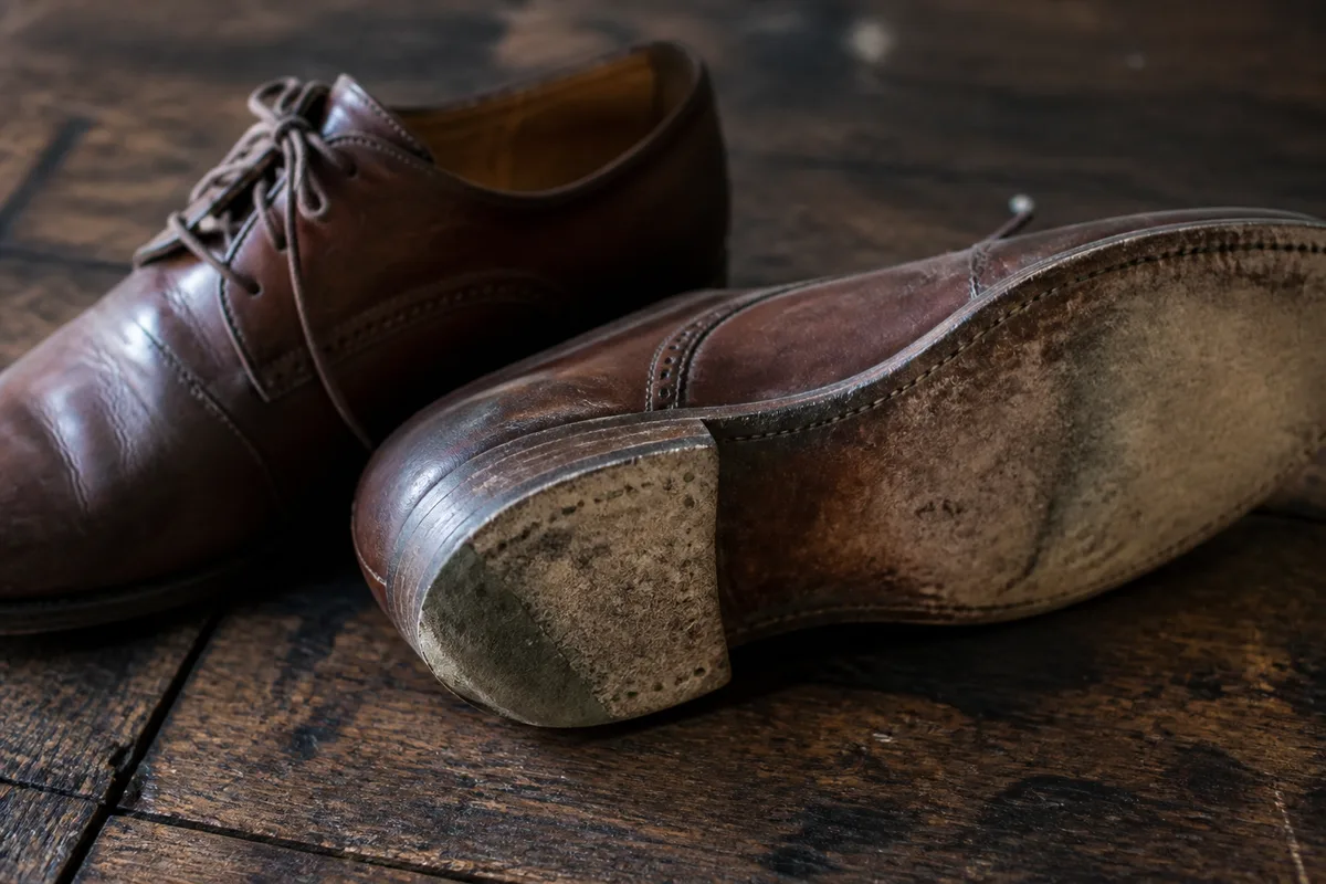Chaussures de ville en cuir usagées posées sur un établi, semelles visibles montrant l’usure inégale